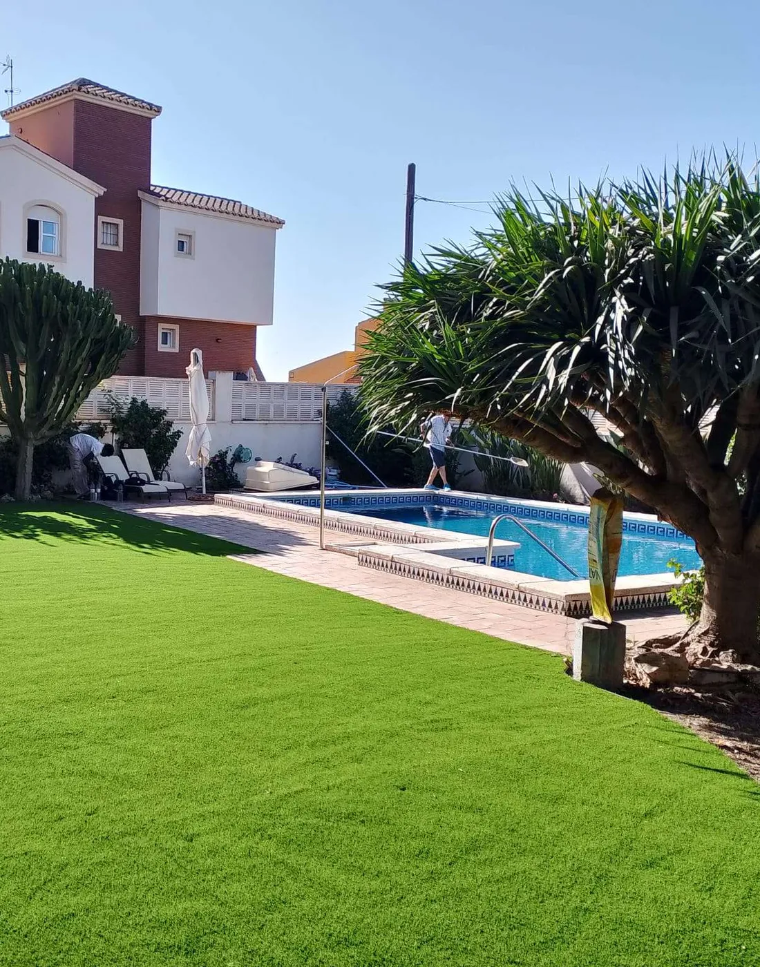 Jardín con césped artificial y una piscina al fondo