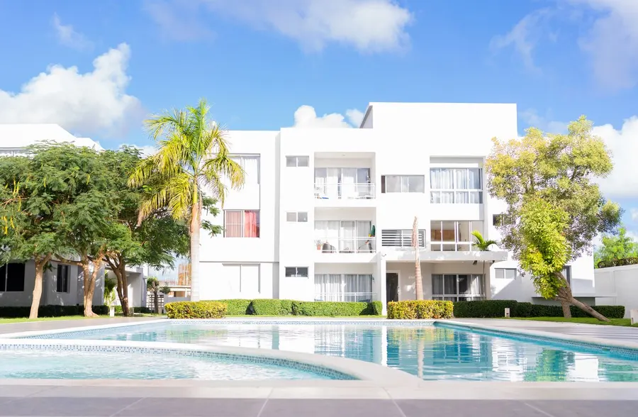 Edificio de apartamentos blanco con piscina comunitaria y jardín
