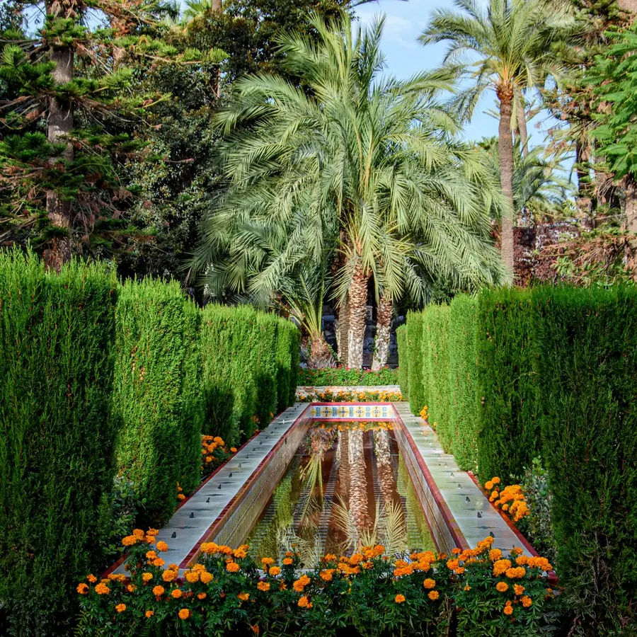 Jardín mediterráneo con palmeras, setos recortados, estanque y flores